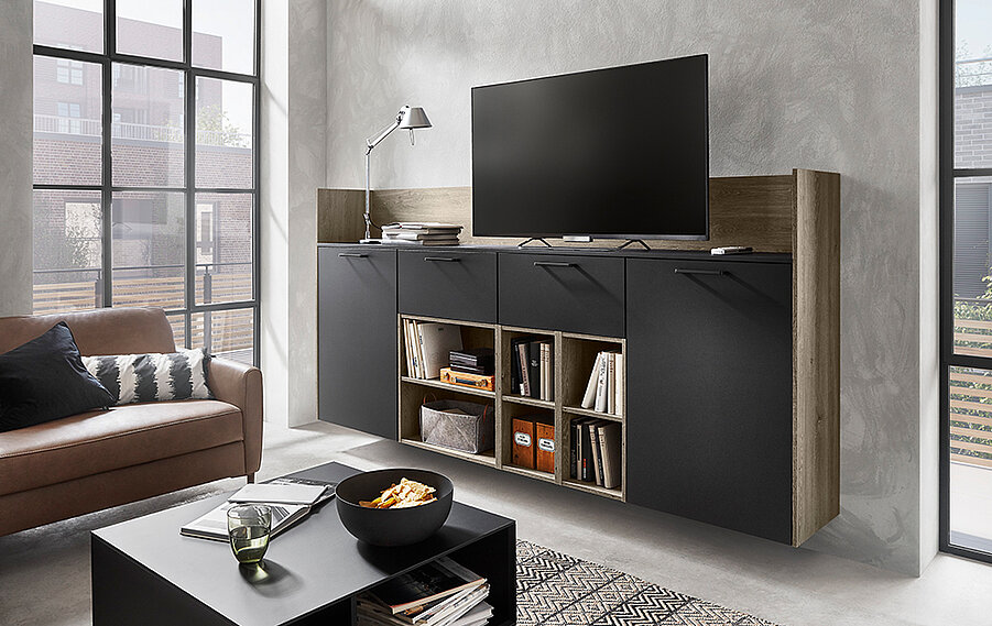 Sala de estar moderna con una elegante unidad de entretenimiento negra con un televisor montado, complementada por un cómodo sofá marrón y elegantes paredes de concreto.