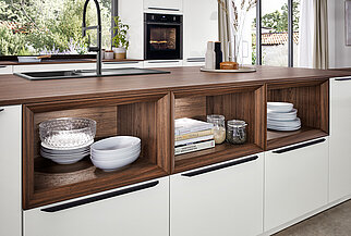 Una elegante cocina con gabinetes blancos con detalles de madera oscura, estanterías organizadas y electrodomésticos integrados, resaltando una mezcla de diseño moderno y practicidad.