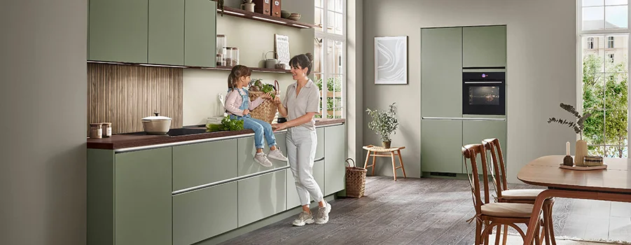 Moderne Küchengestaltung mit sauberen weißen Schränken, einer zentralen Insel und einer Person, die in einem hellen, luftigen Raum mit Stadtblick durch große Fenster kocht.