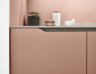 Hedendaags keukenontwerp met een strakke aanrechtblad met minimalistische decoratie tegen een zachte roze achtergrond, waarbij functionaliteit wordt gecombineerd met een moderne esthetiek.