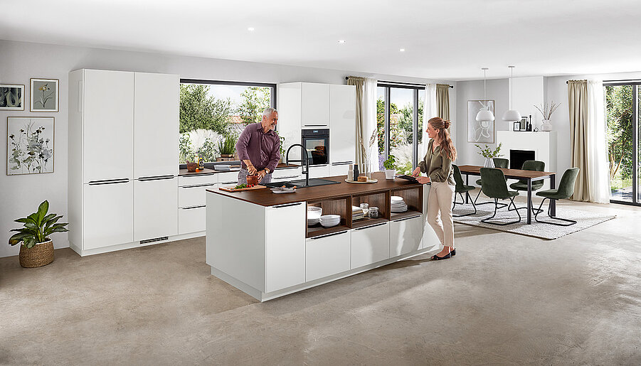 Sophisticated, bright kitchen with two people chatting by an island, featuring sleek white cabinets and contemporary appliances.