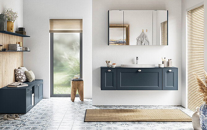 Un elegante interior de baño cuenta con un tocador doble en un tono azul clásico, complementado por un piso de azulejos y una vista tranquila inspirada en la naturaleza.