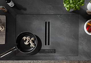 Piano cottura a induzione moderno con design elegante, con una padella con funghi circondata da utensili da cucina minimalisti e erbe fresche.