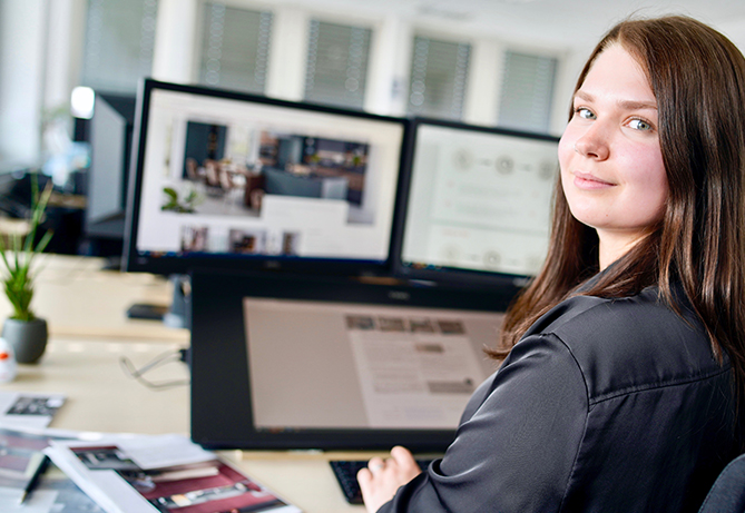 Eine professionelle Frau in einem Büro mit zwei Monitoren, die in ihrer Arbeit vertieft ist und Konzentration sowie Geschäftseffizienz verkörpert.