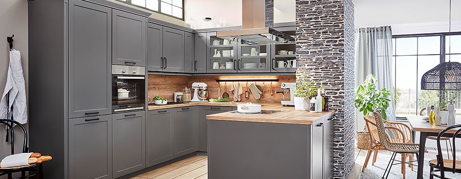 Ruime moderne keuken met grijze kasten, houten werkbladen, roestvrijstalen apparaten en een stijlvolle stenen accentmuur, aangevuld met natuurlijk licht en groen.