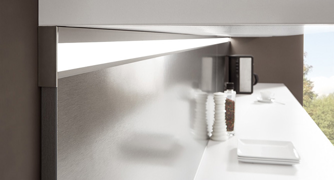 Intérieur de cuisine moderne avec des armoires en acier inoxydable élégantes au design minimaliste, des comptoirs blancs éclatants et une cafetière mise en valeur par la lumière naturelle.