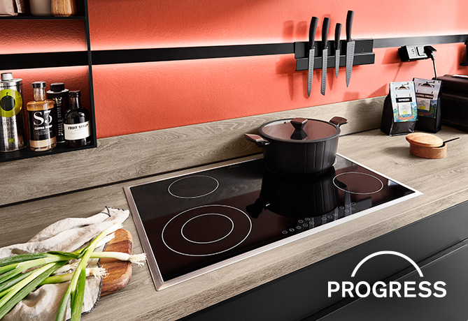 Moderne keuken met een inductiekookplaat met een zwarte pan, omringd door strakke werkbladen en stijlvol georganiseerde kookgerei en ingrediënten.