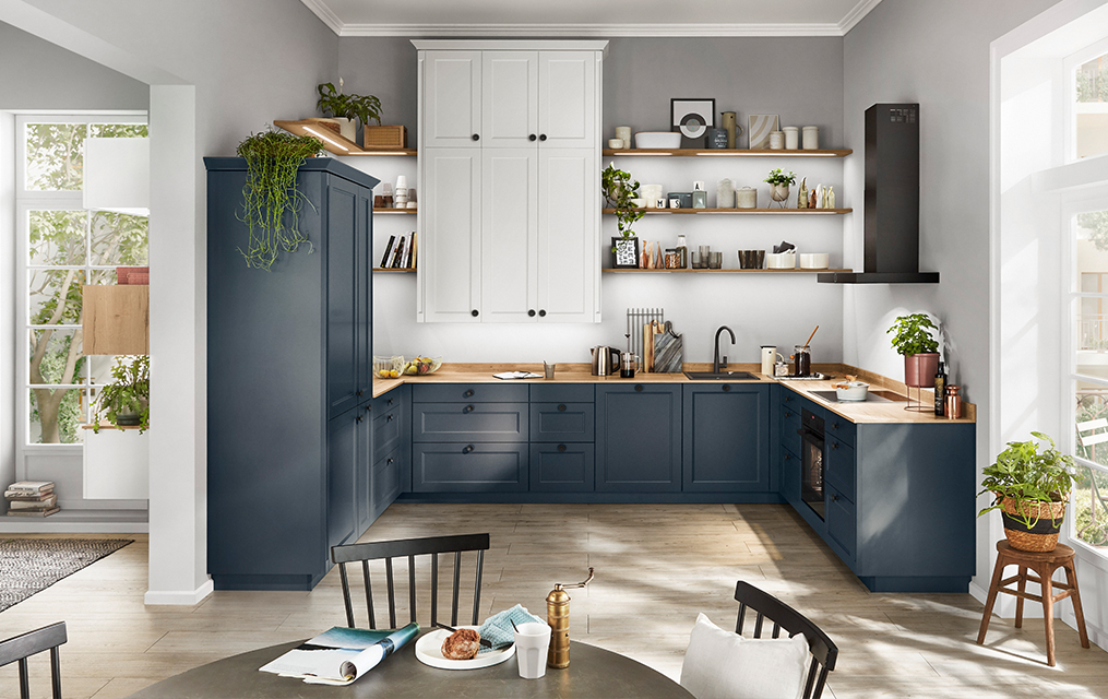 Moderne keuken met blauwe kasten, houten werkbladen en strakke apparaten in een lichte, luchtige ruimte met natuurlijk licht.