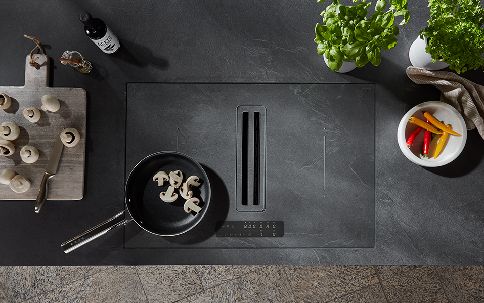 A sleek, modern kitchen setup featuring an induction cooktop, fresh vegetables, and a black frying pan with mushrooms, exemplifying contemporary cooking design.