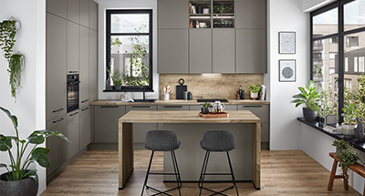 Intérieur de cuisine moderne avec des armoires grises élégantes, des accents en bois et des appareils en acier inoxydable, complétés par la lumière naturelle et la verdure.