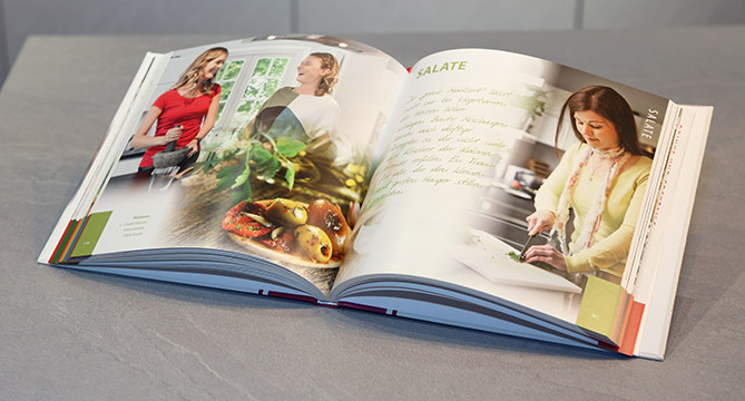 Libro de cocina abierto en una encimera de cocina con fotografías coloridas de comida y una persona cocinando, ilustrando instrucciones de recetas claras y atractivas.