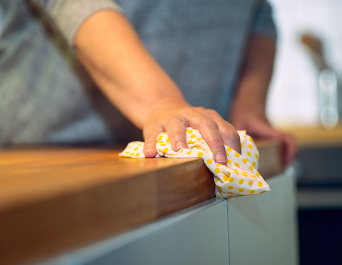 Person wiping a kitchen countertop with a yellow patterned cloth, focusing on cleanliness and household maintenance.