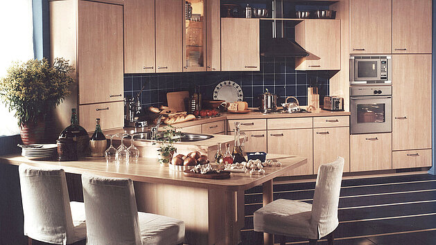 Helle Holz-Küche mit nobilia modernen Geräten, einem großen Tisch und liebevoll angerichtetem Geschirr.