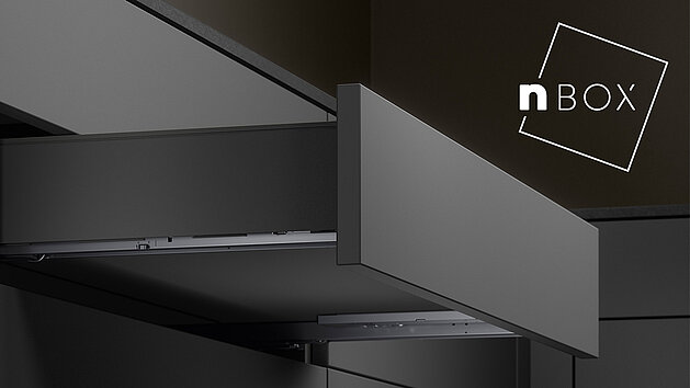 Schwarzer nobilia Küchenschrank mit einem ausgezogenen Grauschubladen, neben dem Logo „nBOX“.