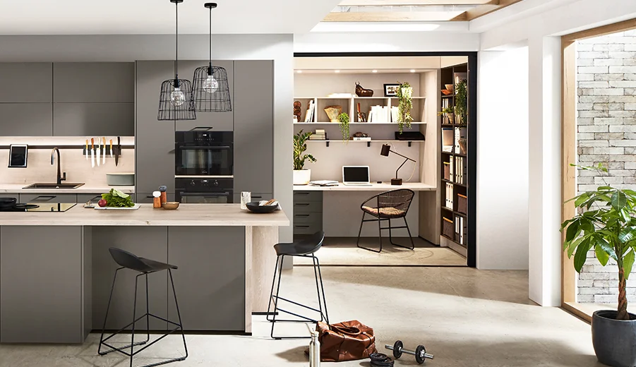 Laser (414) / Eiche Montreal Nachbildung (126) Moderne offene Küche mit eleganten Schränken und einer Insel, die zu einem gemütlichen Homeoffice mit Bücherregalen führt, beleuchtet von natürlichem und Pendelleuchten.