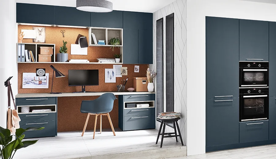 Easytouch (966) Modernes Homeoffice-Setup mit einem eleganten Schreibtisch, wandmontierten Regalen und einer Küchenzeile mit dunkelblauen Schränken und eingebauten Geräten.