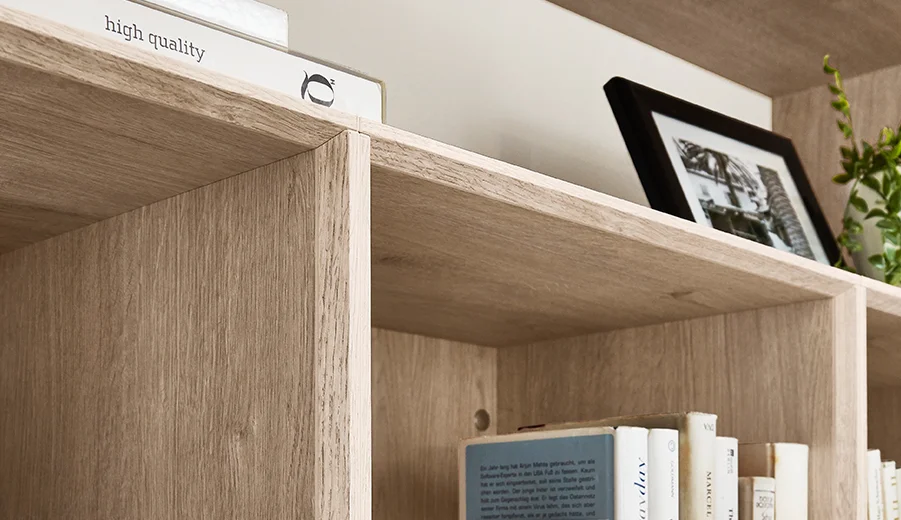 Eiche Montreal Nachbildung (126) Elegante Holzregale zeigen verschiedene Bücher, ein gerahmtes Foto und eine dekorative Schachtel mit einem Etikett "hochwertig", was auf einen anspruchsvollen und organisierten Raum hinweist.
