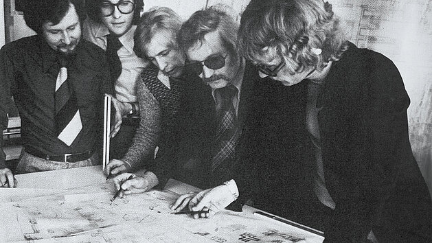 Fünf Fachleute von nobilia analysieren einen detaillierten Architekturplan auf einem Tisch im Jahr 1973.
