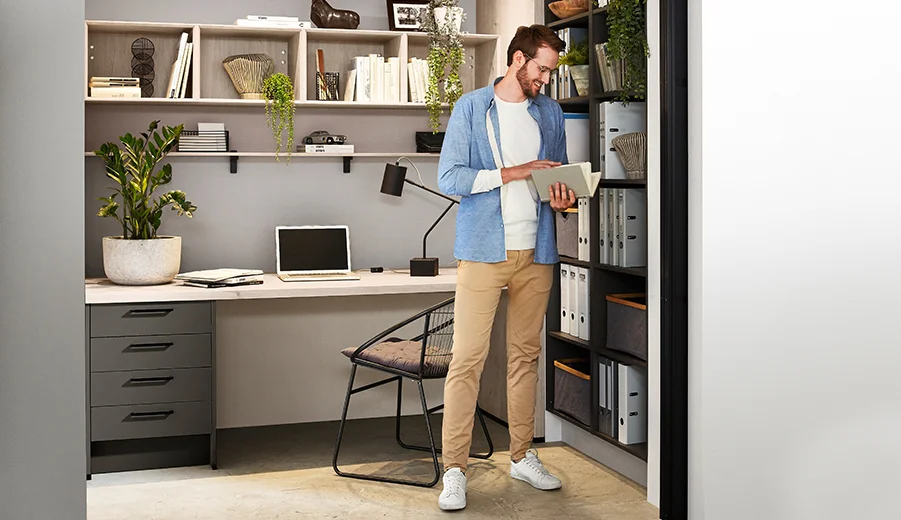 Laser (414) / Eiche Montreal Nachbildung (126) Ein konzentrierter Einzelner in einem stilvollen Home-Office-Setup, der durch ein Buch an einem organisierten Regal blättert und eine Mischung aus Komfort und Produktivität widerspiegelt.